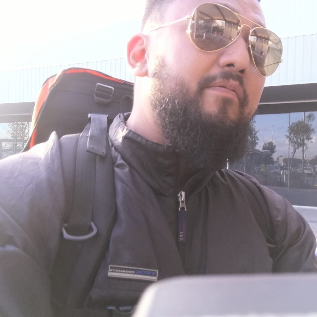 Man with sunglasses and backpack outdoors near a pool area, sunny day.