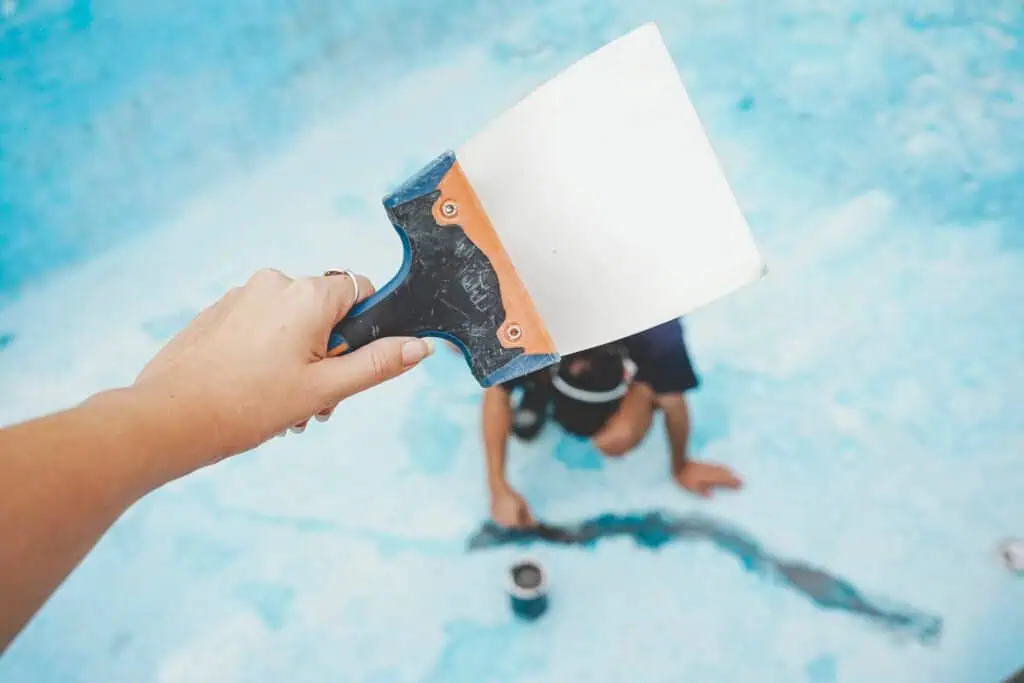 Pool cleaning tool in hand with a person swimming in the background.